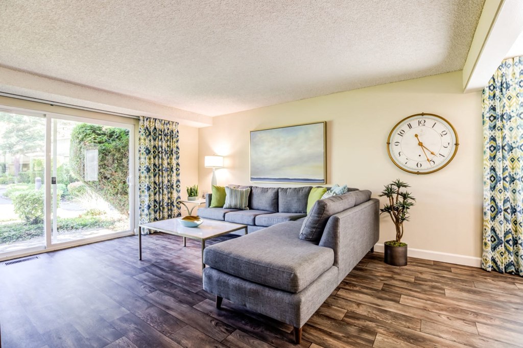 A living room with a grey couch, a coffee table, a painting, a clock, and a potted plant.